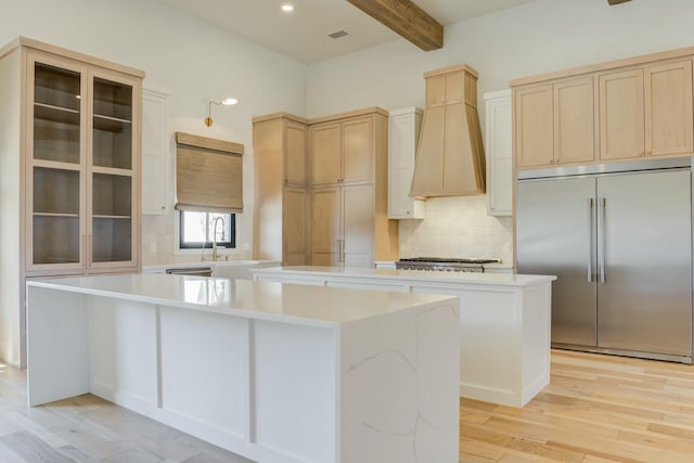 kitchen with beam ceiling, custom exhaust hood, backsplash, appliances with stainless steel finishes, and a kitchen island