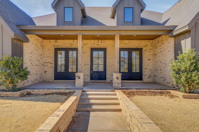 property entrance featuring brick siding, roof with shingles, board and batten siding, and french doors