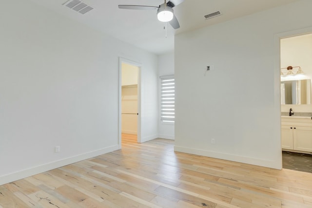 unfurnished bedroom featuring light wood finished floors, visible vents, a walk in closet, and a sink