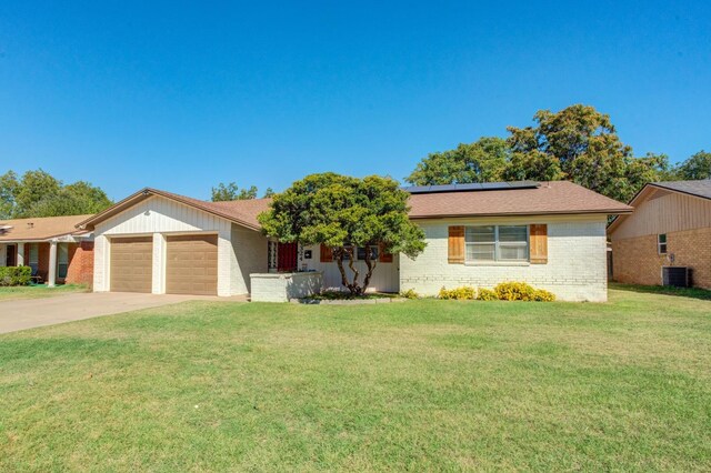 ranch-style home featuring an attached garage, solar panels, brick siding, concrete driveway, and a front lawn