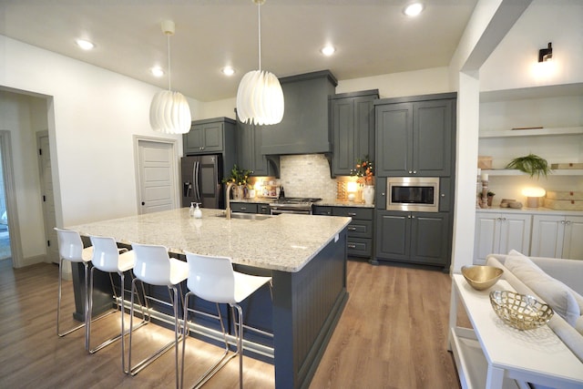 kitchen with light stone counters, a sink, stainless steel appliances, wood finished floors, and backsplash