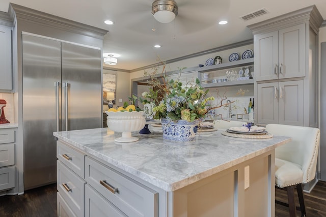 kitchen featuring light stone counters, stainless steel built in fridge, a kitchen island, visible vents, and dark wood-type flooring