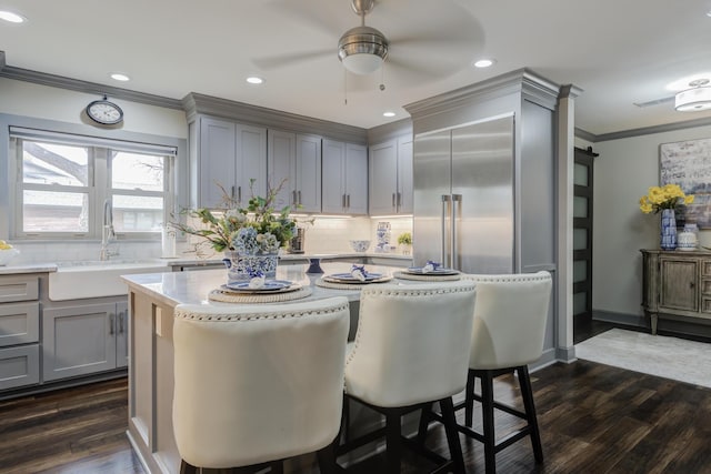 kitchen with a sink, gray cabinets, ceiling fan, backsplash, and ornamental molding