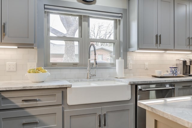 kitchen featuring stainless steel dishwasher, gray cabinetry, a sink, and backsplash