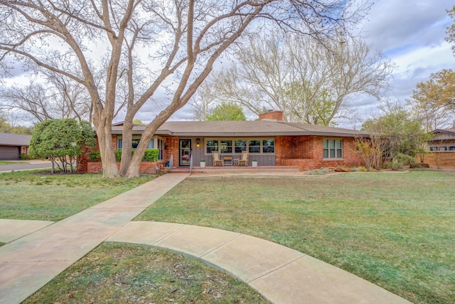 ranch-style home featuring a chimney, brick siding, a porch, and a front lawn