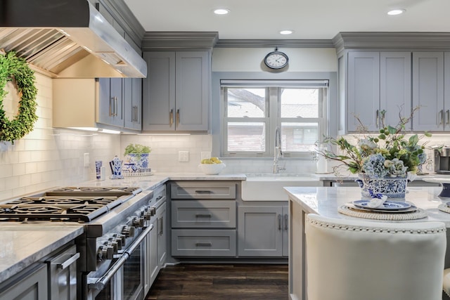 kitchen with range with two ovens, gray cabinets, wall chimney range hood, and a sink