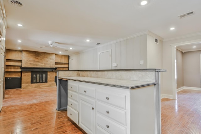 kitchen with a large fireplace, white cabinets, ceiling fan, crown molding, and light hardwood / wood-style flooring