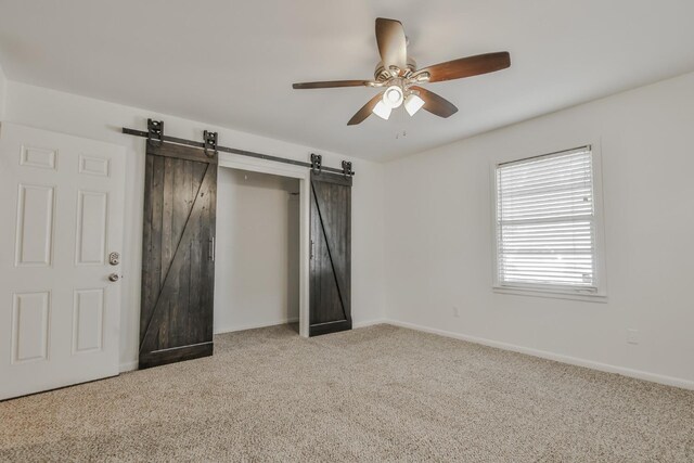 unfurnished bedroom with light colored carpet, a barn door, and ceiling fan