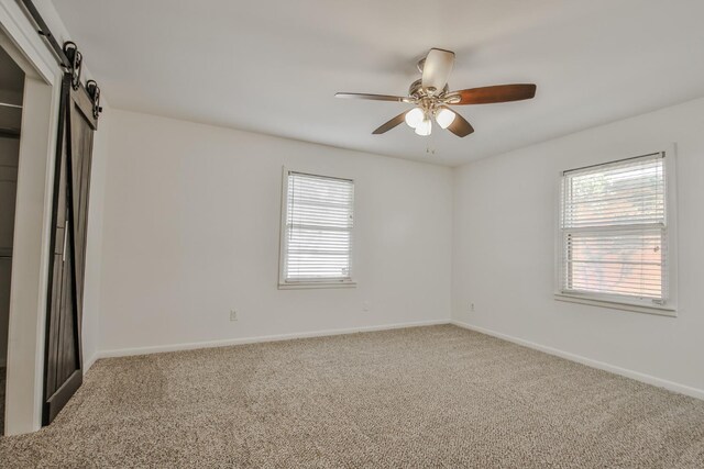 unfurnished bedroom with a barn door, ceiling fan, and carpet