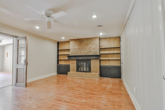 unfurnished living room with hardwood / wood-style floors, a stone fireplace, ornamental molding, and ceiling fan