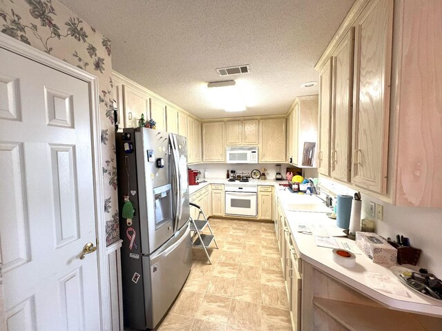 kitchen with light brown cabinetry, sink, white appliances, and a textured ceiling