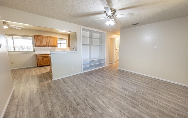 unfurnished living room featuring a textured ceiling, built in shelves, ceiling fan, and light wood-type flooring