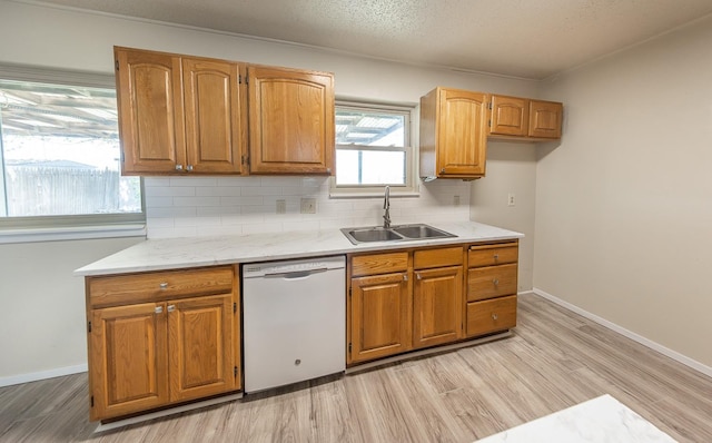 kitchen featuring sink, tasteful backsplash, a textured ceiling, light wood-type flooring, and white dishwasher