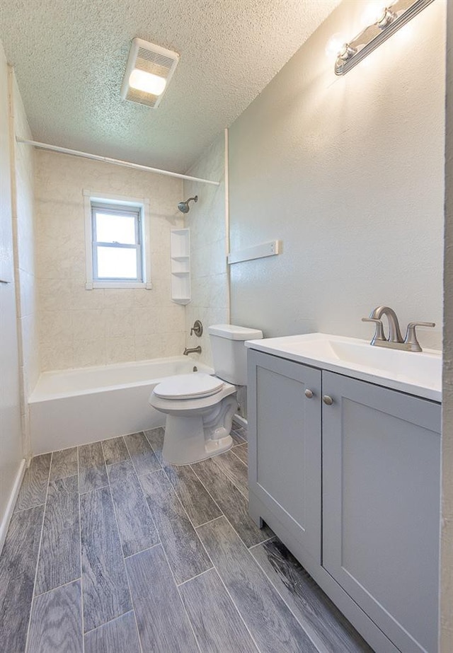 full bathroom with tiled shower / bath, vanity, toilet, and a textured ceiling