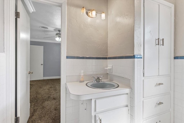 bathroom featuring ceiling fan, tile walls, vanity, ornamental molding, and a textured ceiling