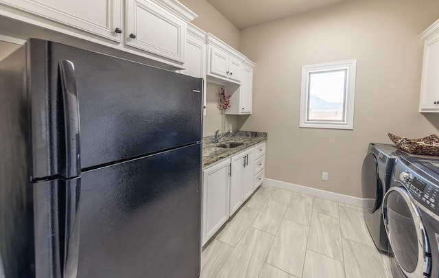 kitchen with white cabinets, washing machine and clothes dryer, a sink, and freestanding refrigerator