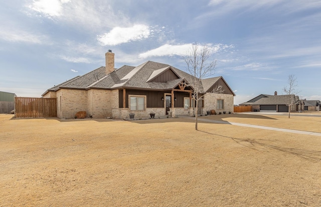 view of front of property with roof with shingles, a chimney, stone siding, and fence