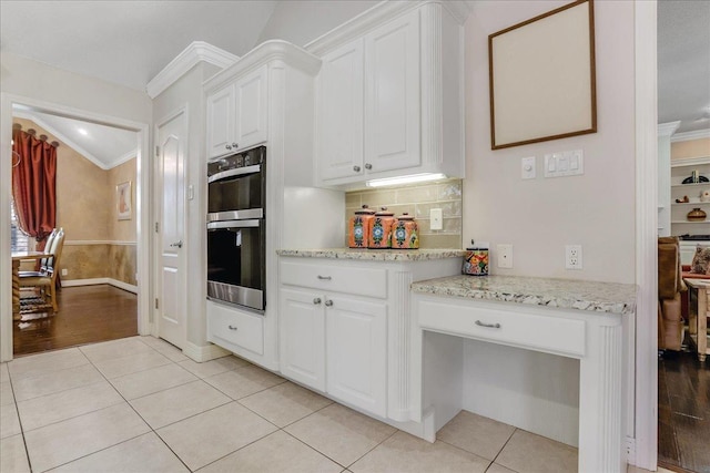 kitchen with white cabinetry, stainless steel double oven, crown molding, and light tile patterned floors