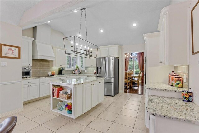 kitchen featuring decorative light fixtures, stainless steel fridge, custom range hood, a kitchen island, and white cabinets