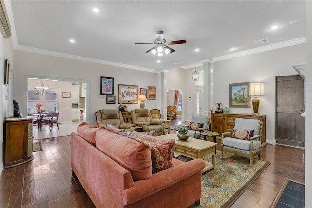 living room featuring decorative columns, ornamental molding, dark wood-type flooring, and ceiling fan with notable chandelier