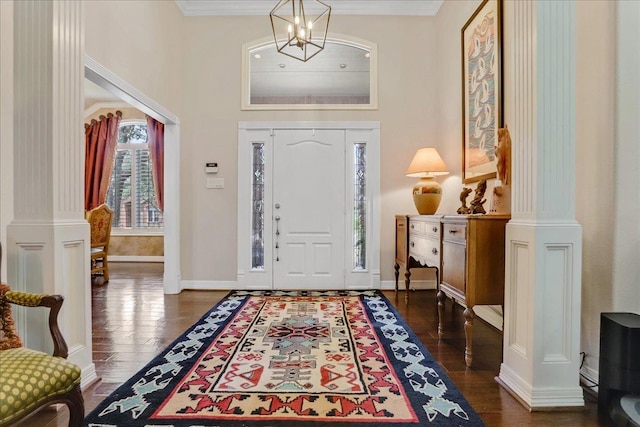 entrance foyer with dark hardwood / wood-style flooring, ornamental molding, a chandelier, and ornate columns