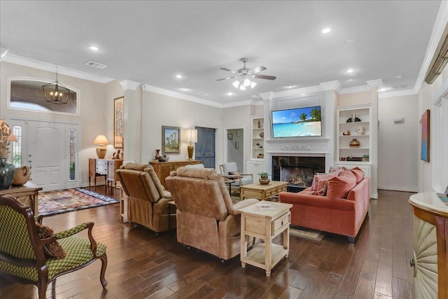 living room featuring ceiling fan with notable chandelier, decorative columns, dark hardwood / wood-style flooring, crown molding, and built in shelves