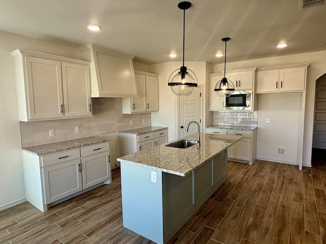 kitchen featuring stainless steel microwave, a kitchen island with sink, sink, and white cabinets