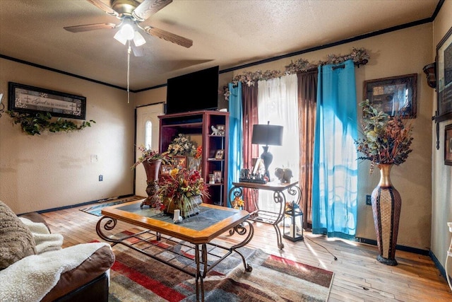 living room featuring crown molding, a ceiling fan, wood-type flooring, and a textured ceiling