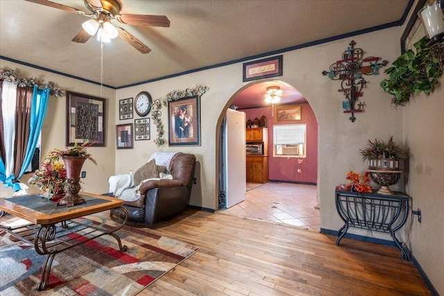 interior space with crown molding, light wood-style flooring, arched walkways, a textured ceiling, and a ceiling fan