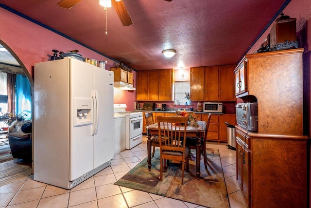 kitchen featuring white appliances, brown cabinetry, light tile patterned flooring, ceiling fan, and under cabinet range hood