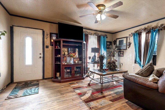 living room with ornamental molding, a textured ceiling, a ceiling fan, and wood-type flooring