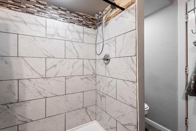 full bath featuring toilet, tiled shower, and a textured wall