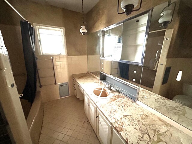 full bathroom with shower / bathtub combination with curtain, tile walls, tile patterned flooring, vanity, and toilet