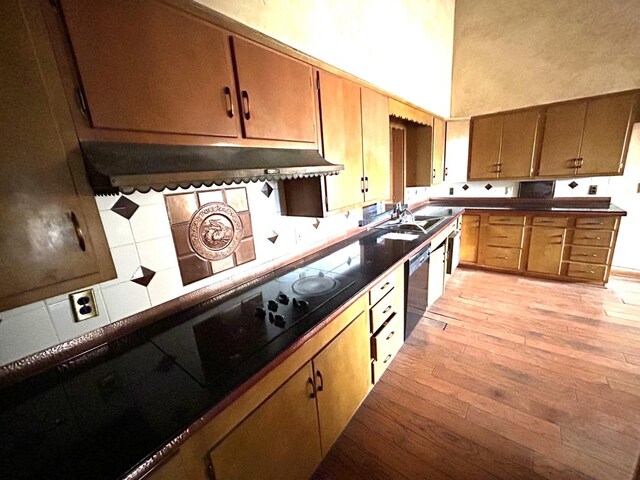 kitchen with dishwashing machine, sink, a towering ceiling, decorative backsplash, and light wood-type flooring