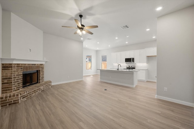 unfurnished living room with ceiling fan, a fireplace, sink, and light wood-type flooring