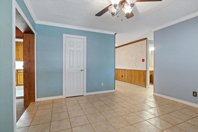 unfurnished room with ornamental molding, wooden walls, ceiling fan, and a textured ceiling