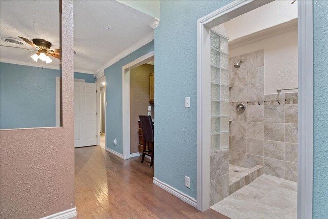 bathroom featuring hardwood / wood-style flooring, ceiling fan, tiled shower, ornamental molding, and a textured ceiling