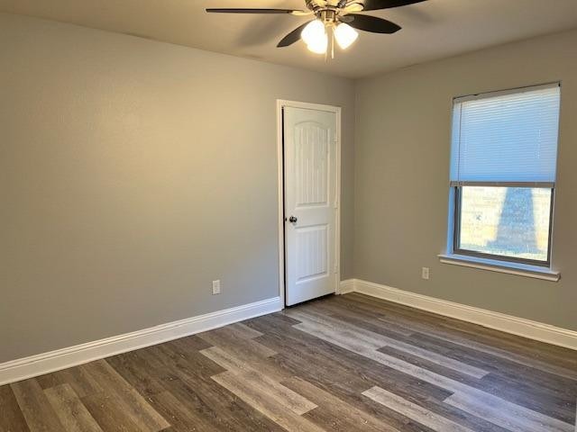 spare room with baseboards, dark wood finished floors, and a ceiling fan