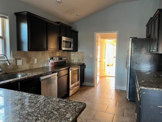 kitchen with lofted ceiling, stainless steel appliances, a sink, dark stone counters, and tasteful backsplash