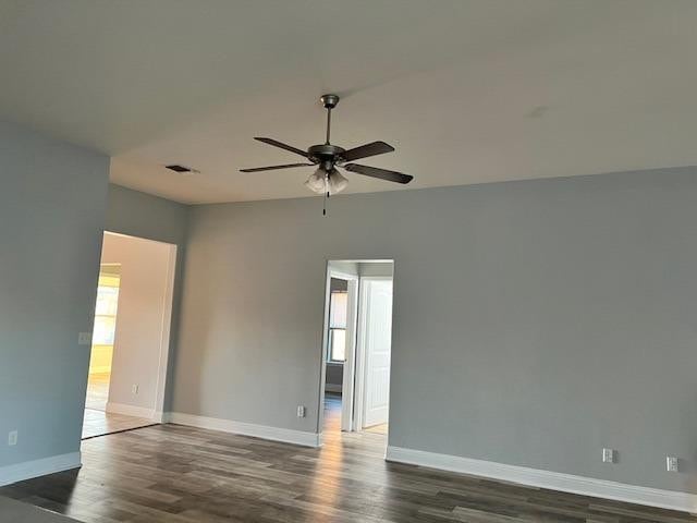 unfurnished room with ceiling fan, dark wood-type flooring, visible vents, and baseboards