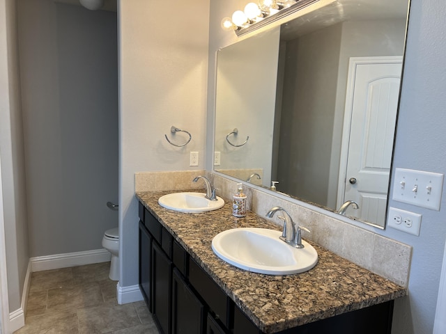 bathroom featuring toilet, double vanity, baseboards, and a sink