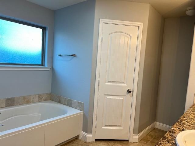 bathroom featuring a garden tub, vanity, and baseboards