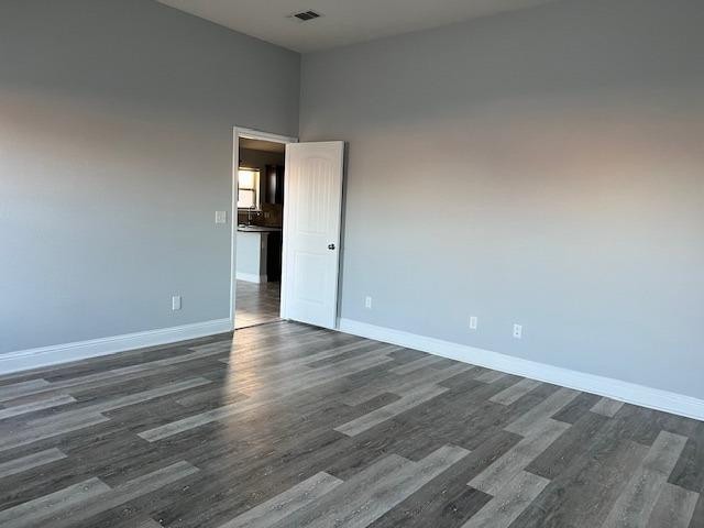 spare room featuring dark wood-style floors, visible vents, and baseboards