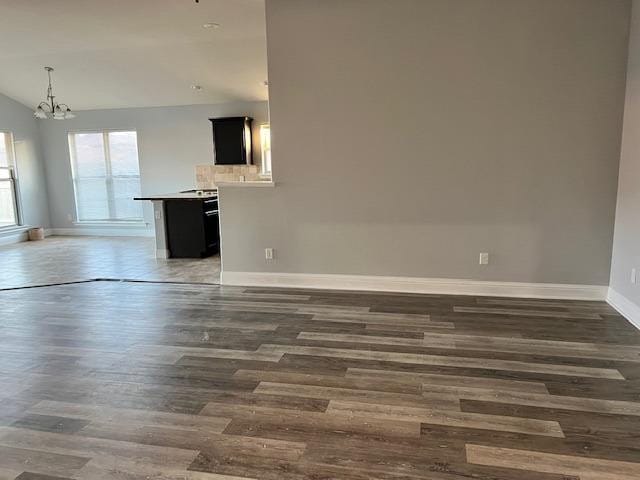 unfurnished living room featuring vaulted ceiling, dark hardwood / wood-style floors, and a chandelier