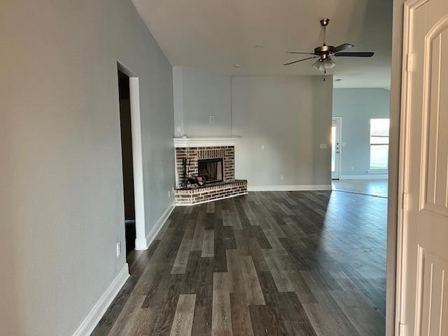 unfurnished living room featuring ceiling fan, lofted ceiling, dark hardwood / wood-style floors, and a brick fireplace