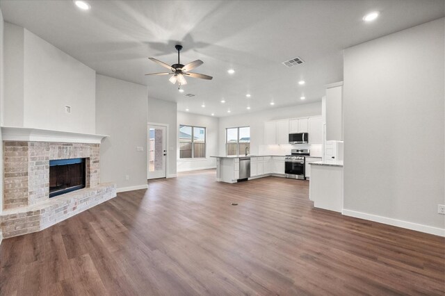 unfurnished living room featuring hardwood / wood-style flooring, ceiling fan, and a brick fireplace