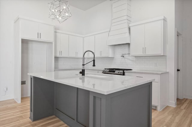 kitchen featuring decorative light fixtures, light hardwood / wood-style floors, white cabinets, and a center island with sink