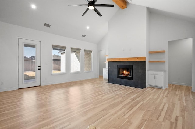 unfurnished living room featuring high vaulted ceiling, beamed ceiling, a tiled fireplace, ceiling fan, and light hardwood / wood-style flooring