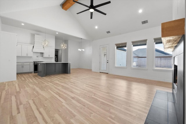 unfurnished living room featuring beamed ceiling, ceiling fan with notable chandelier, high vaulted ceiling, and light hardwood / wood-style flooring