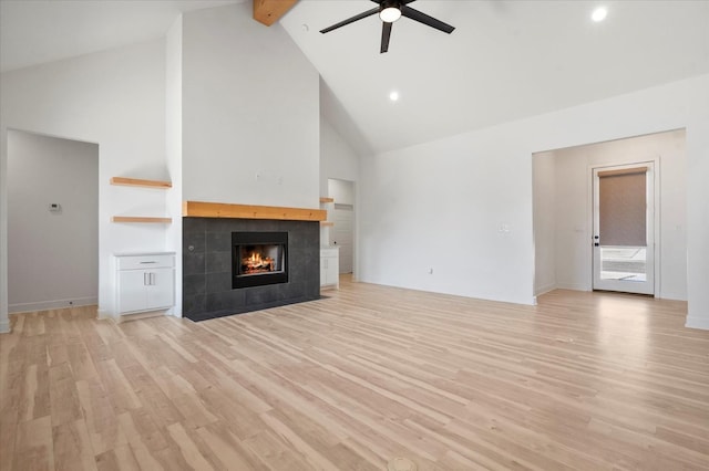 unfurnished living room featuring a tiled fireplace, light wood-type flooring, high vaulted ceiling, and beam ceiling